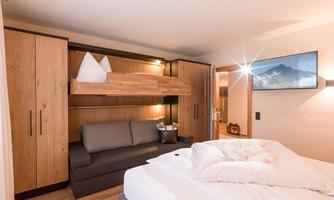 A cozy bedroom with a double bed, a sofa bed, and a bunk bed. The wooden furniture and soft lighting create an inviting atmosphere.