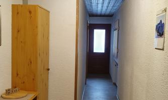 A bright hallway with wooden ceilings and simple wall design. On the left stands a wooden wardrobe, and at the end of the hallway is a door.