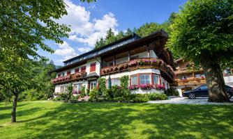 A picturesque house with blooming balconies surrounded by green meadows. The clear sky and trees create an idyllic atmosphere.