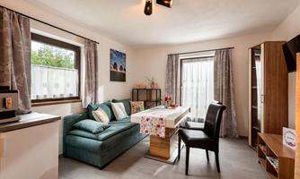 A cozy living room with a green sofa and a dining table. The windows are decorated with curtains and there are some decorative elements.