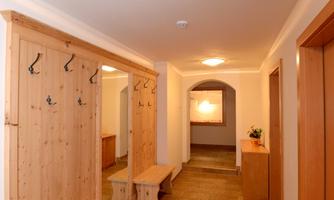 A bright hallway with a wooden bench and coat rack. The walls are light and the floor is covered with tiles.