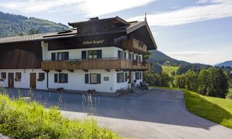 A charming mountain house with wooden cladding and balconies. Surrounded by green meadows and gentle hills under a clear sky.