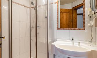 A modern bathroom with a shower and a sink. The walls are tiled in white, and there are wood details in the room.
