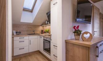 A modern kitchen with white cabinets and wood paneling. It has windows with daylight and a cozy atmosphere.