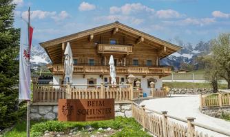 A traditional wooden house in the Alps with a cozy outdoor area. Surrounded by magnificent mountains and green grass.