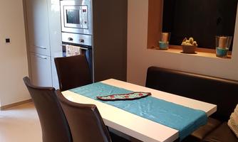 A modern dining room with a white table and brown chairs. In the background, a refrigerator and an oven can be seen.