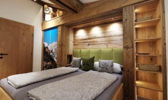 A cozy bedroom with wooden design and a large double bed. The walls are decorated in warm tones and there is a nice lighting.