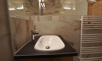 A modern bathroom with a white sink and a wood surface. The walls are clad with high-quality tiles.