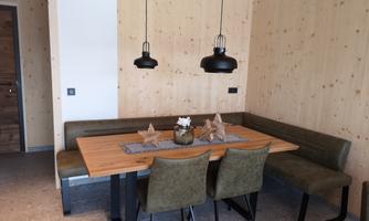A modern dining room with a wooden table and comfortable benches. The walls are clad in light wood and simple, stylish lamps hang over the table.