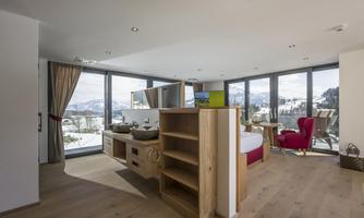 A modern room with large windows offering a view of the mountains. The decor is minimalist and cozy, with a warm wooden floor.