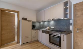 A modern kitchen with light cabinets and a dark countertop. The floor is made of wood and there is a door to the next room.
