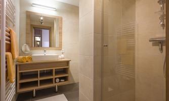 A modern bathroom with a shower and wooden shelves. There are towels in warm colors and a large mirror.