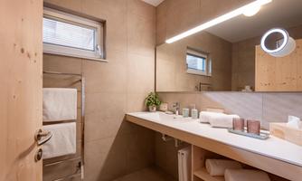 A modern bathroom with a bright design and wooden surfaces. Towels and toiletries are visible on the shelf.