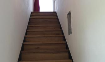 A wooden staircase leads upward. At the end of the staircase is a door with a red curtain and a window that lets in light.
