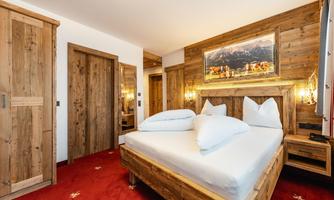 A cozy bedroom with a wooden bed and red carpet. The walls are equipped with wood paneling, and a landscape painting hangs above the bed.