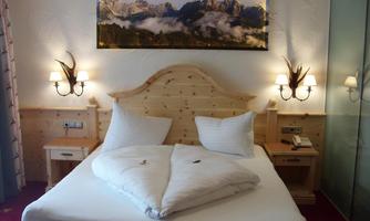 A cozy bedroom with a double bed and wooden furniture. On the wall hangs a picture of mountains with clouds.