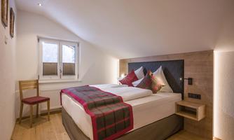 A modern bedroom with a double bed and wood-paneled walls. The room is bright and cozy, with a small table and chair.