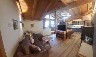 A modern living room with a wooden ceiling and large windows. There is a sofa, a television, and a dining area with a table and chairs.