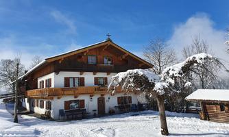 A traditional house in the snow with a beautiful balcony.  
Surrounded by snow-covered trees and a clear blue sky.