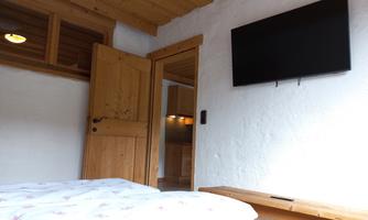 A cozy room with a wooden door and a modern flat-screen TV on the wall. The room has a bright, friendly atmosphere with wooden elements.