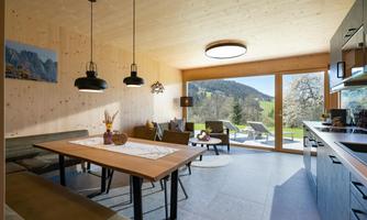 A modern living room with wooden walls and large windows. The room is bright and offers a view of nature.