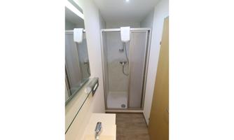 A modern bathroom with a shower cabin and a mirror. The walls are light and the floor is in neutral tones.
