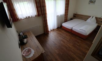 A cozy room with a double bed and wooden floor. On the table, there is a coffee pot and a small decoration.