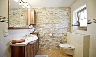 A modern bathroom with wooden cabinets and a stone wall. The room is bright and comfortably designed.