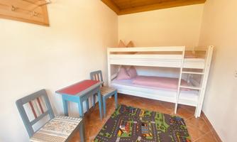 A small room with a bunk bed and a colorful rug. There is a table and two chairs, in a cozy and child-friendly style.