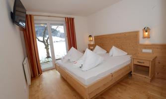 A cozy room with a double bed and wooden decor. Large windows provide a view of the outdoor scenery.