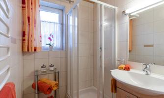 A modern bathroom with a shower and a sink. Towels in warm colors and a window with a view of flowers give the room an inviting atmosphere.