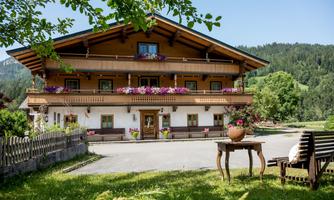 A charming house in alpine style with colorful flowers on the balconies. Surrounded by green landscape and mountains in the background.