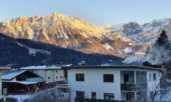 A picturesque winter landscape with snow-covered mountains in the background. In the foreground stands a modern residential house.