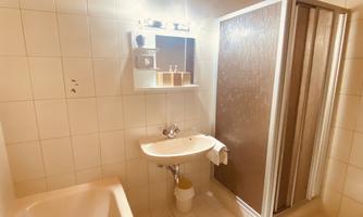 A simple bathroom with a bathtub and a shower. On the wall, there is a mirror with care products.