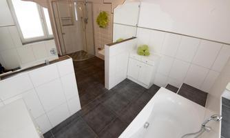 A modern bathroom with a bathtub and a shower. The walls are tiled, and there are fresh towels in light green.