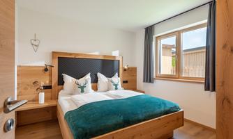 A modern bedroom with a wooden double bed and pillows featuring deer motifs. Large windows let in plenty of light and create an inviting atmosphere.