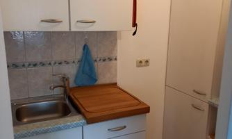 A small kitchen with a sink, wooden countertop, and a refrigerator. A blue dish towel hangs on the wall.