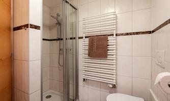 A modern bathroom with a shower cabin and white tiles. There is a towel rack and toilet in the corner.