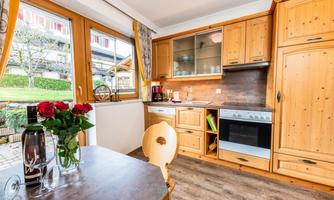 A cozy kitchen with wooden cabinets and large windows. Fresh roses and a bottle of wine are on the table.