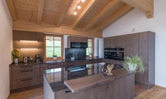 Modern kitchen with wooden ceiling and large windows. It is equipped with elegant furniture and appliances.