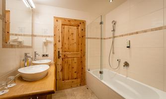 A modern bathroom with wooden details and a bathtub. Two sinks and a large mirror are present.