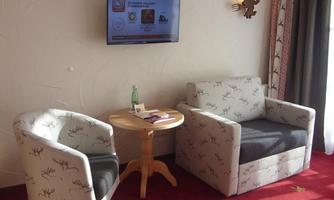 A cozy sitting area with two armchairs and a small table. A TV hangs on the wall and there is a bottle of water on the table.