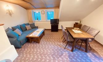 A cozy living space with a blue sofa and a wooden table. The room has a warm, inviting character with a large window.