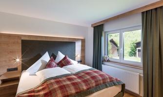 A cozy bedroom with a large bed and red pillows.  
Large windows provide plenty of daylight and a view outside.