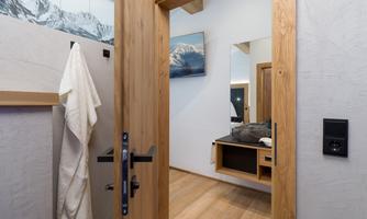 A modernly designed interior door that overlooks a stylish room with wooden flooring and modern furnishings. A towel hangs on the left side.