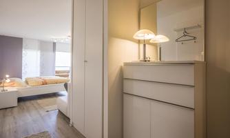A modern bedroom with a white wardrobe and a stylish sideboard. The room is well-lit and has large windows.