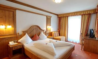 A cozy hotel room with a large bed and stylish wooden decor. There is a window with curtains and a seating area.