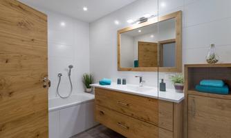 A modern bathroom with a bathtub and a large mirror light. The furniture is made of wood, and colorful towels as well as plants add a fresh accent.