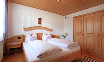 A cozy bedroom with a wooden ceiling and a large double bed. The room features a wardrobe and soft lighting.