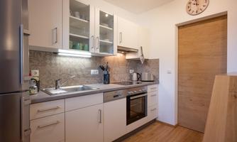 A modern kitchen with gray cabinets and a well-equipped countertop. The room has a warm wooden floor and a bright, inviting atmosphere.